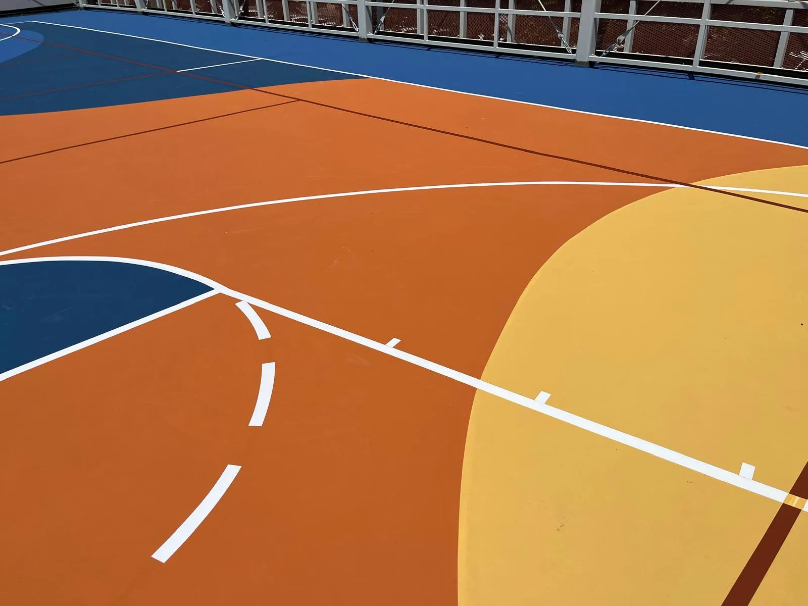 Campo da basket in resina acrilica Mapecoat TNS Multisport Professional, dettaglio delle righe bianche nastrature su campiture arancio, blu e giallo — Liceo Belfiore, Mantova